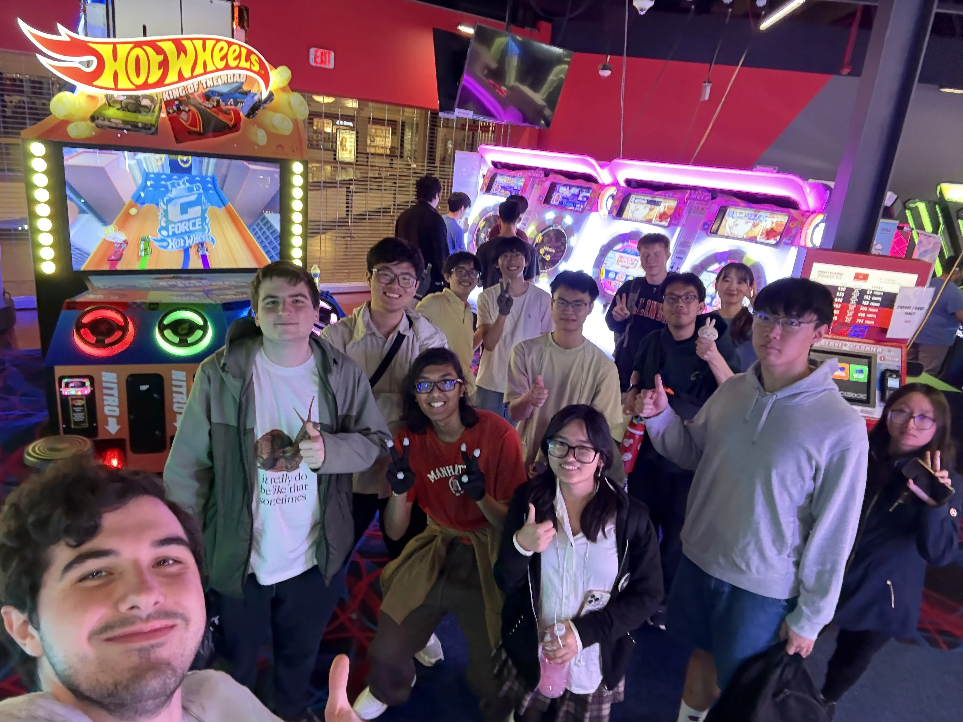 A dozen club members crowded together for a group selfie in front of arcade cabinets on an arcade trip